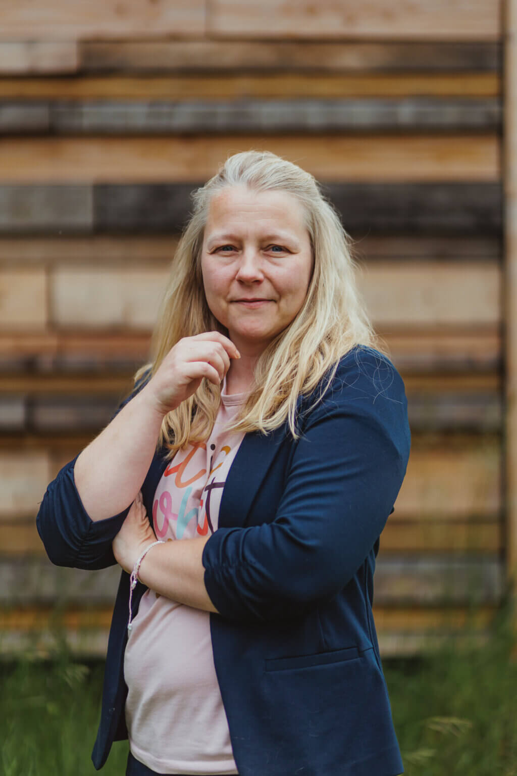 Susann Schlatterer vor einer Holzwand, die Hand nachdenklich am Kinn